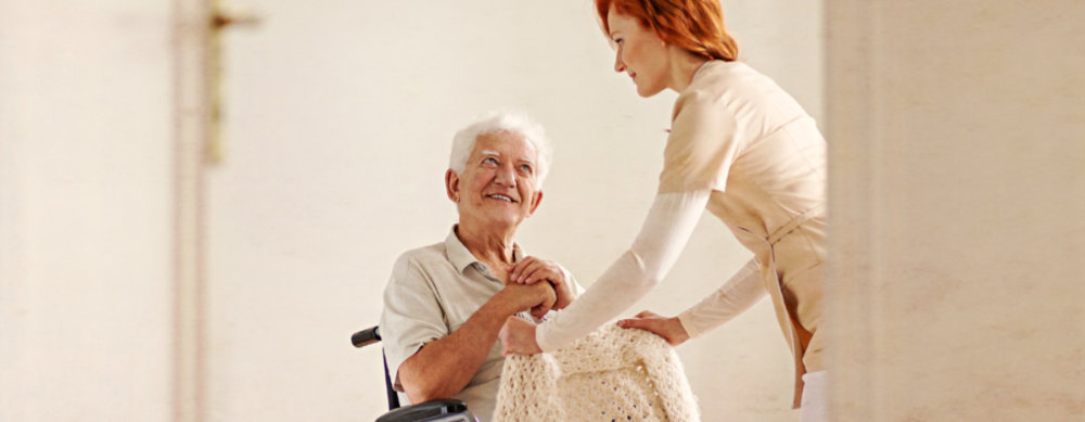a young caregiver helping an elderly gentlemen in a wheelchair